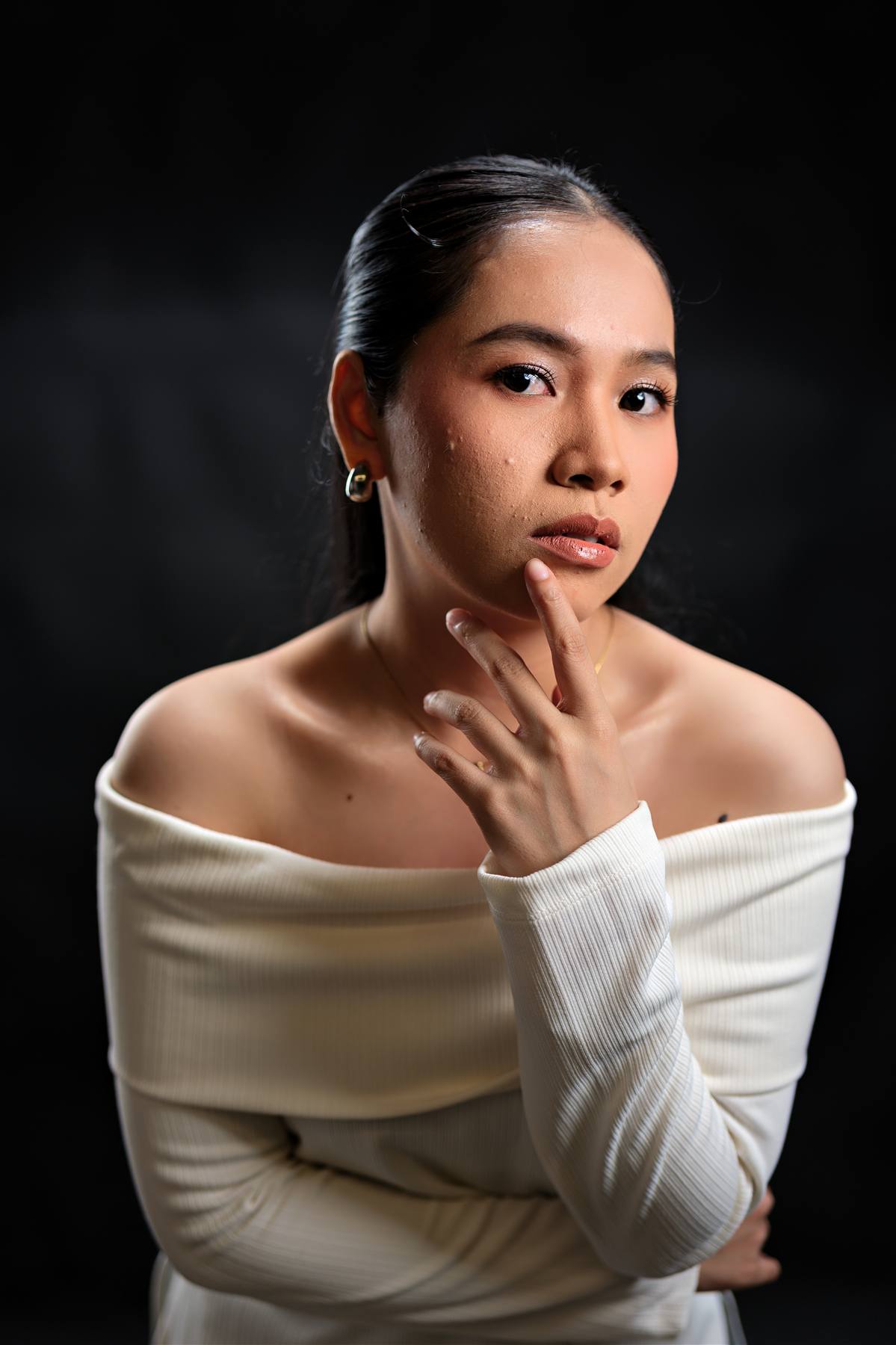 Studio portrait of a woman in a cream off-shoulder sweater against a dark background