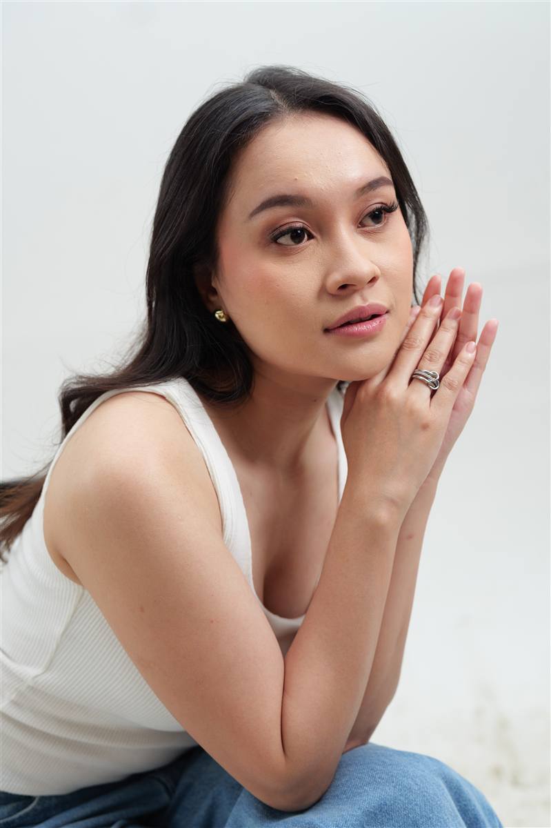 Woman resting her chin on her hand in a white tank top, bright studio
