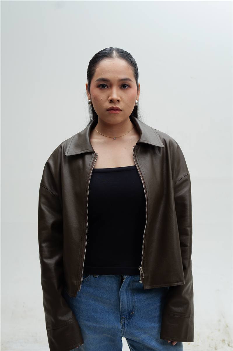 Woman in a leather jacket and jeans against a light grey background