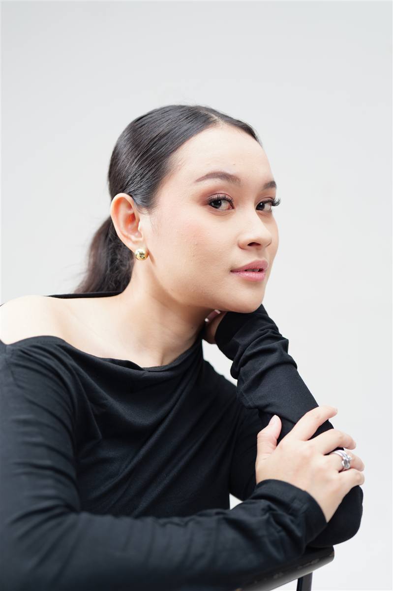 Woman in a black off-shoulder top sitting on a chair, light grey studio