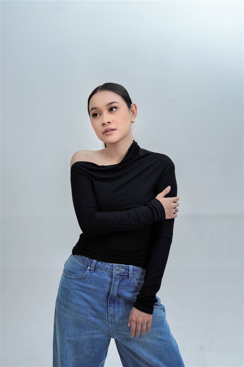 Woman in a black top and jeans standing in a bright studio