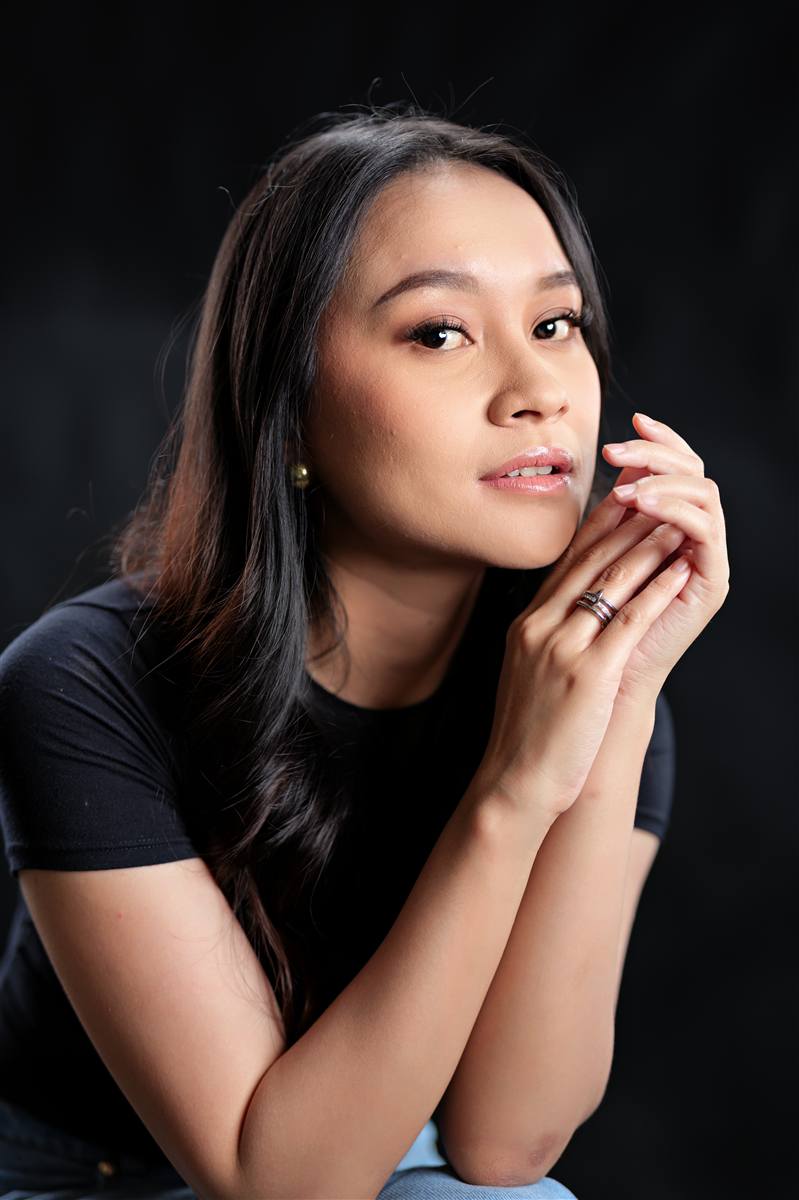 Woman seated with her hands together, low key studio light